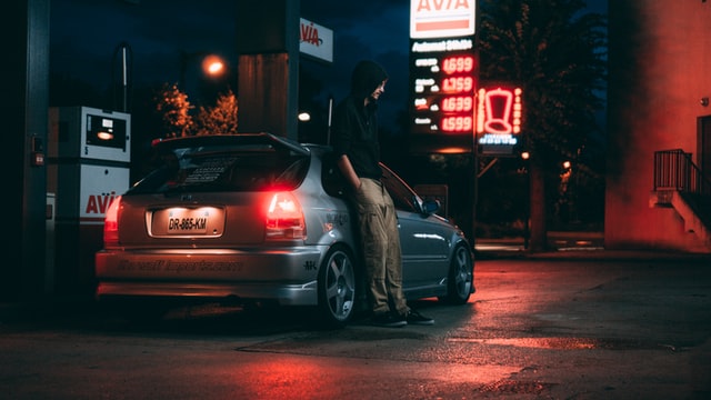 Dark photo of a man standing besides his car at a gas station